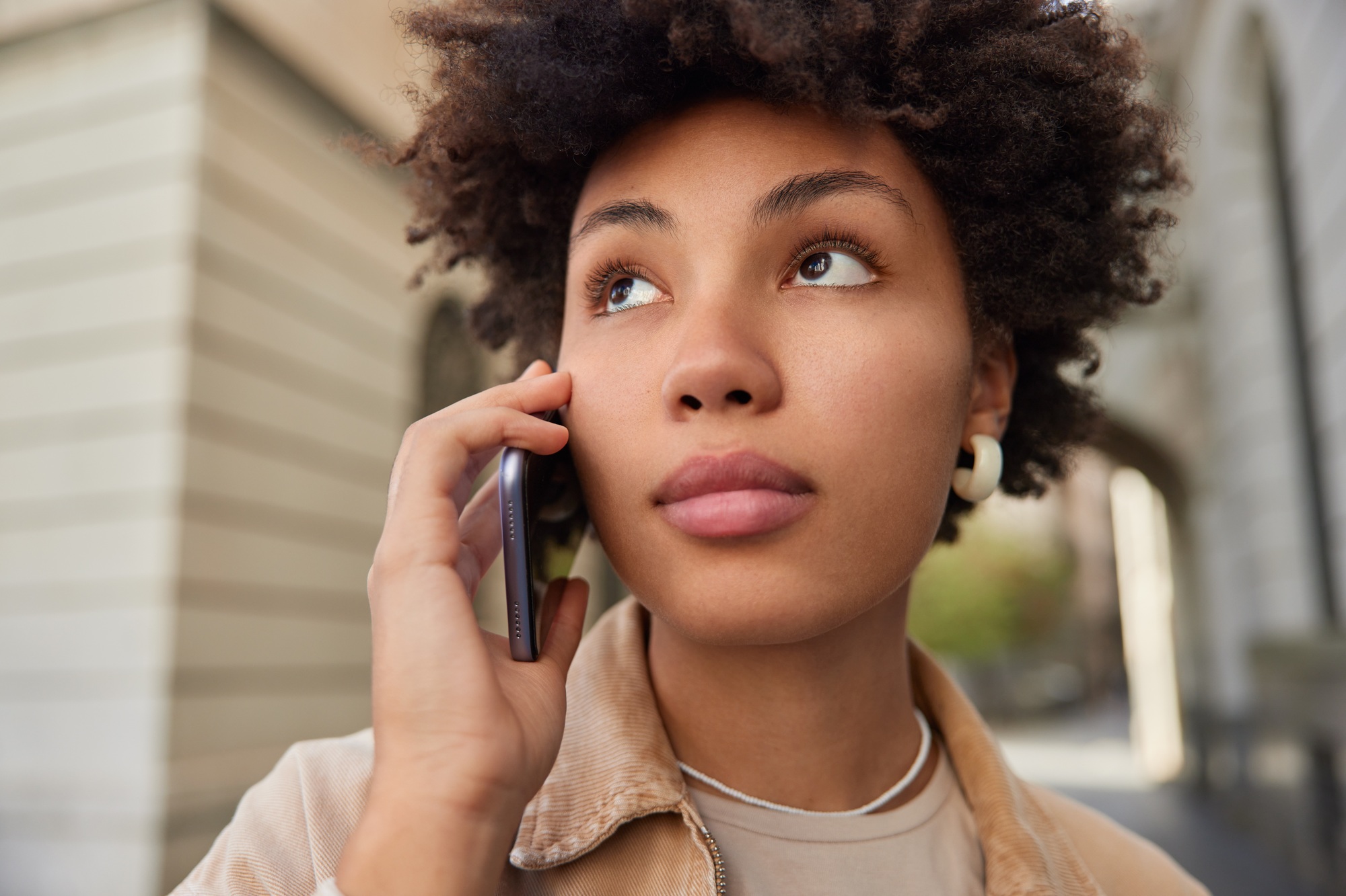 Close up shot of thoughtful African American woman looks away makes telephone call via international