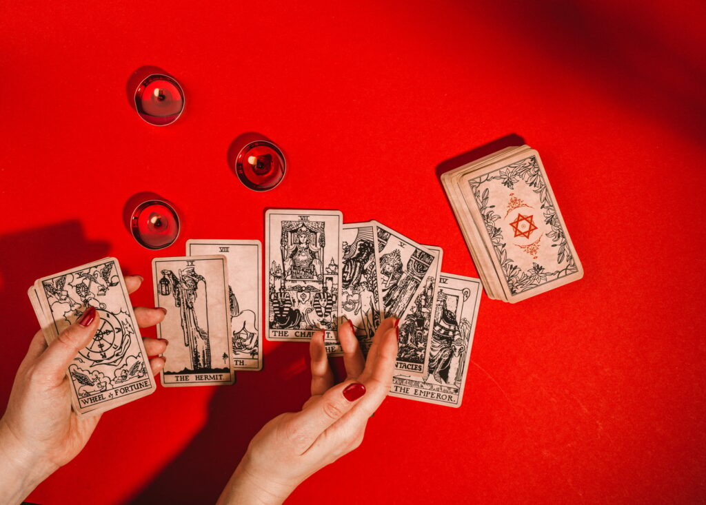 Tarot cards and female hands of fortune teller on red background